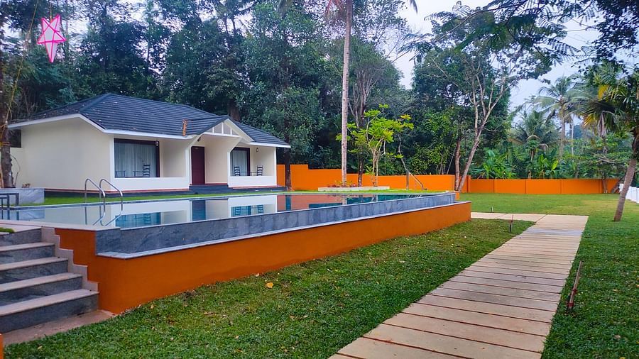 An image of a cottage with a private swimming pool surrounded by a lawn and trees around - Fragnant Nature Kollam